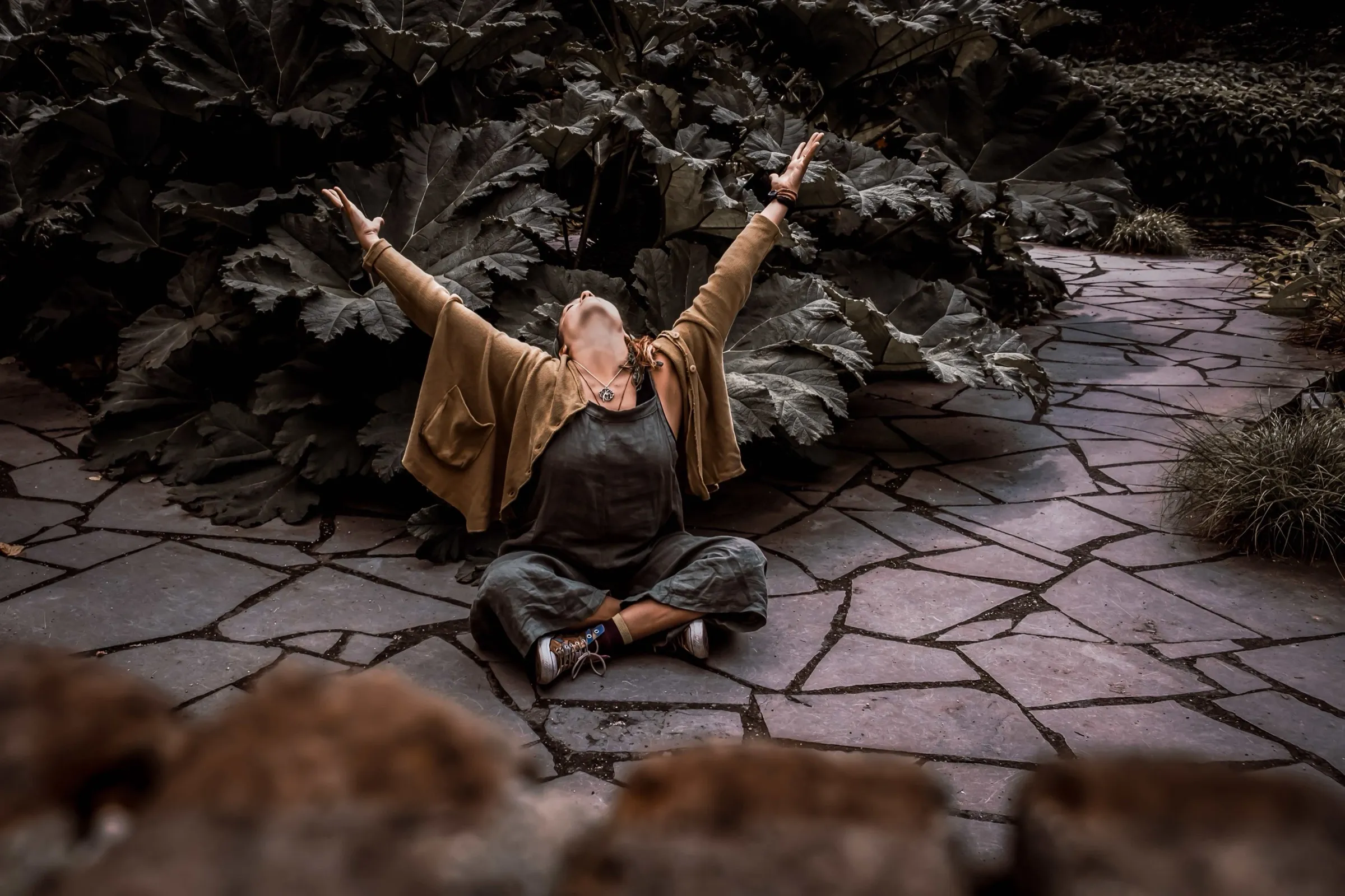Mirella sitting cross-legged on a stone path, arms raised