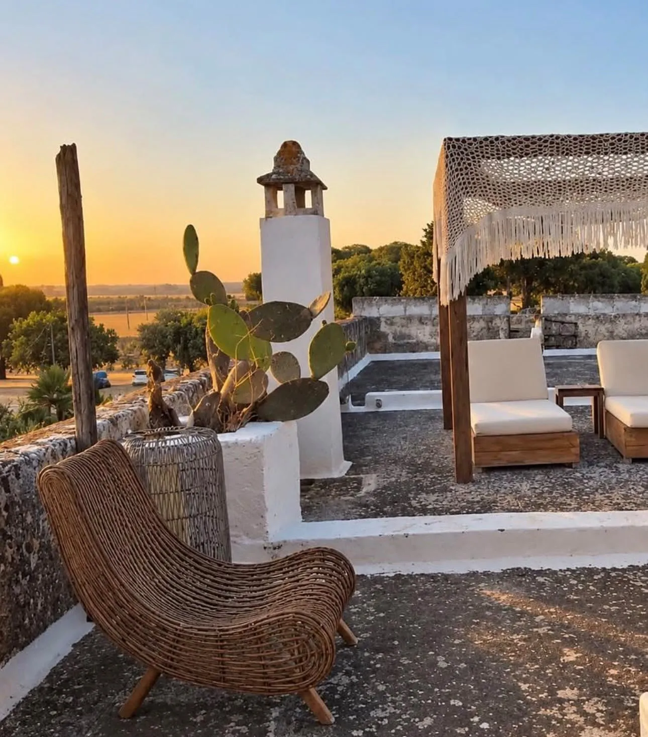 A woven chair and shaded daybeds on the masseria roof terrace at sunset, looking over the Puglian countryside