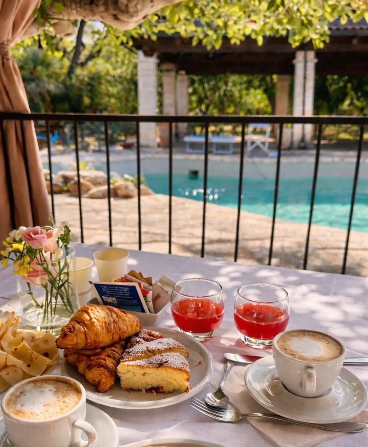 Brunch laid out on a table above the pool, with cappuccinos, croissants and fresh juice